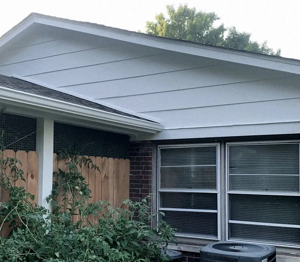 Gable siding painted a clean pale gray-white, white trim and gutter, the same two windows and fence.