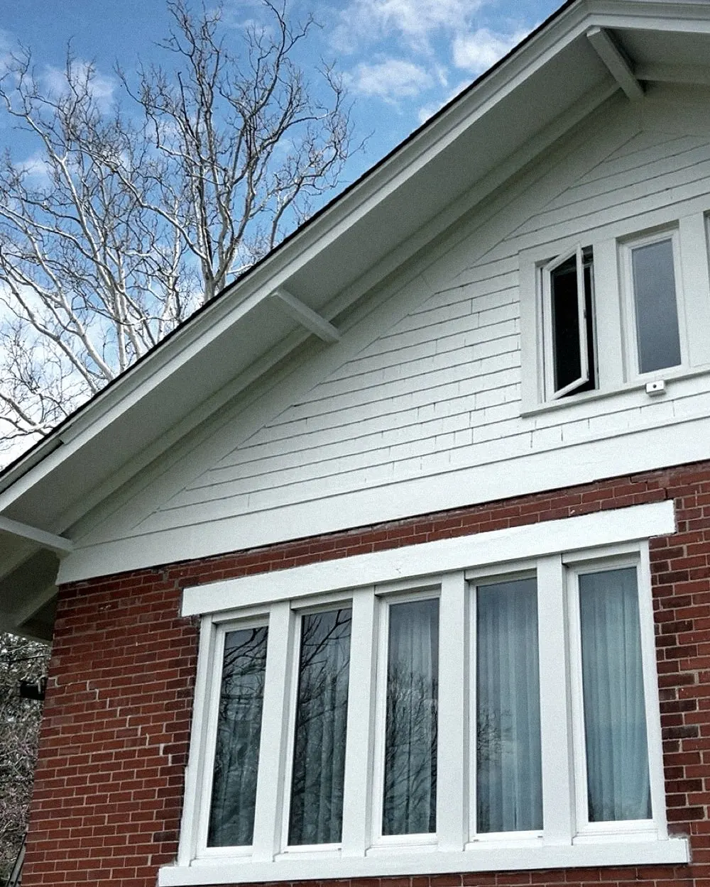 Smooth white gable siding and trim over red brick, a row of white-framed windows.