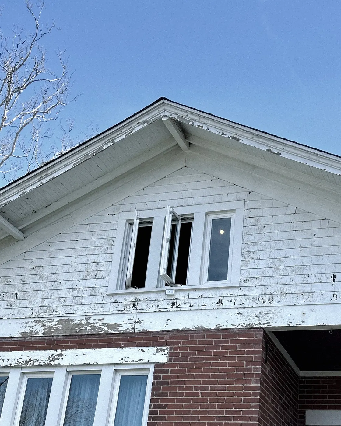 White clapboard gable with paint peeling off the siding and trim, three small windows.