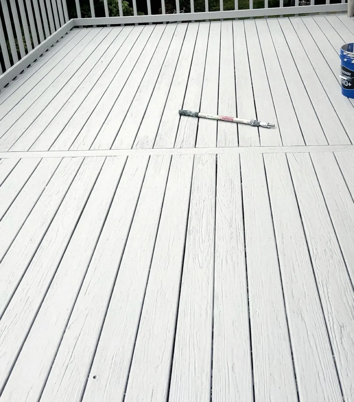 Deck boards in a light gray finish, a paint bucket and a pole at the edge of the frame.
