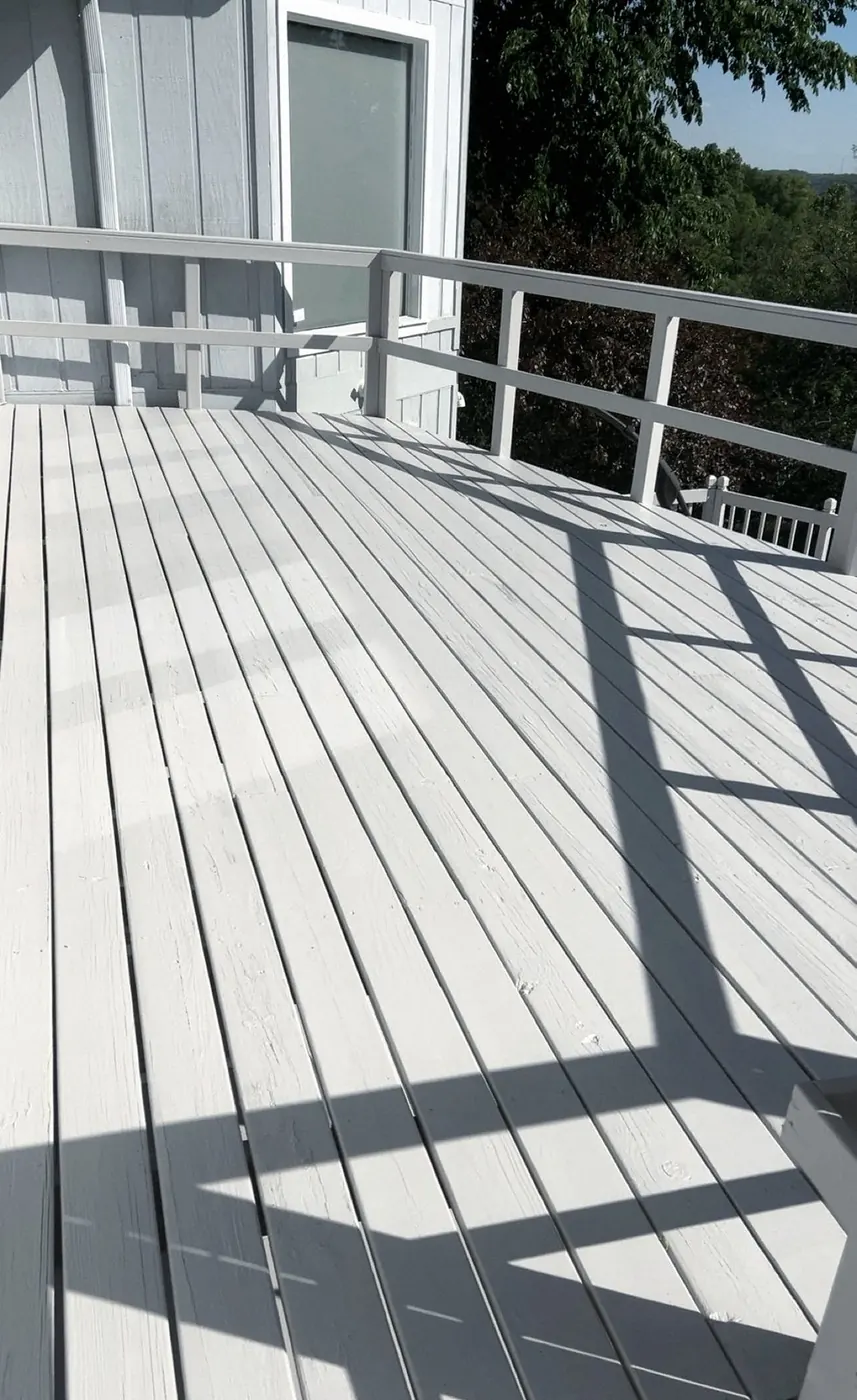 Deck in a smooth pale gray finish, railings repainted, long shadows across the boards.