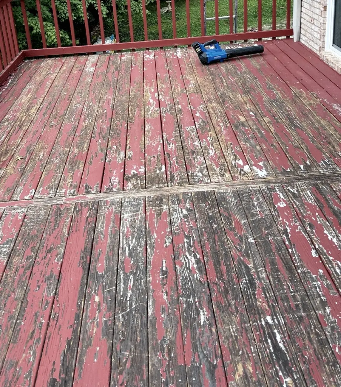 Red-painted deck boards with paint peeling off, a cordless blower lying on the deck.