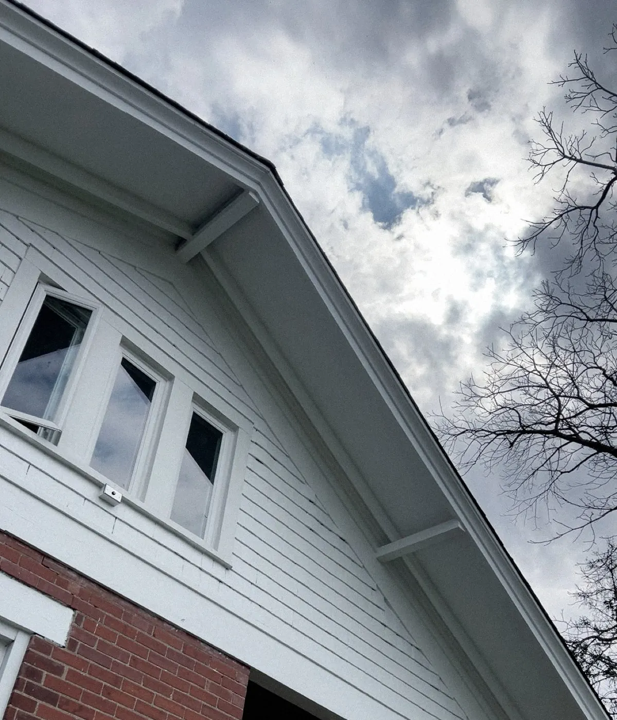 Upward view of a white gable with three windows and clean trim under a cloudy sky.
